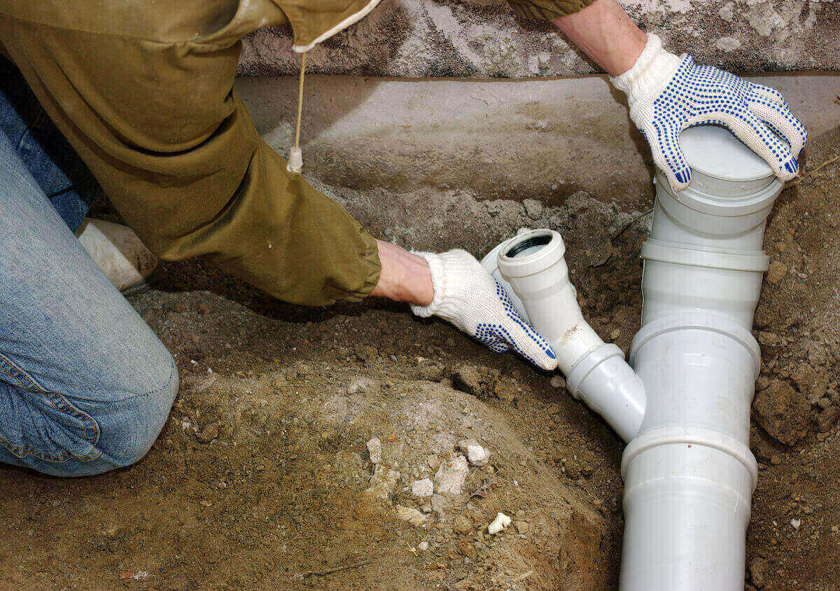 a plumber setting up white sewage pipes under a persons home