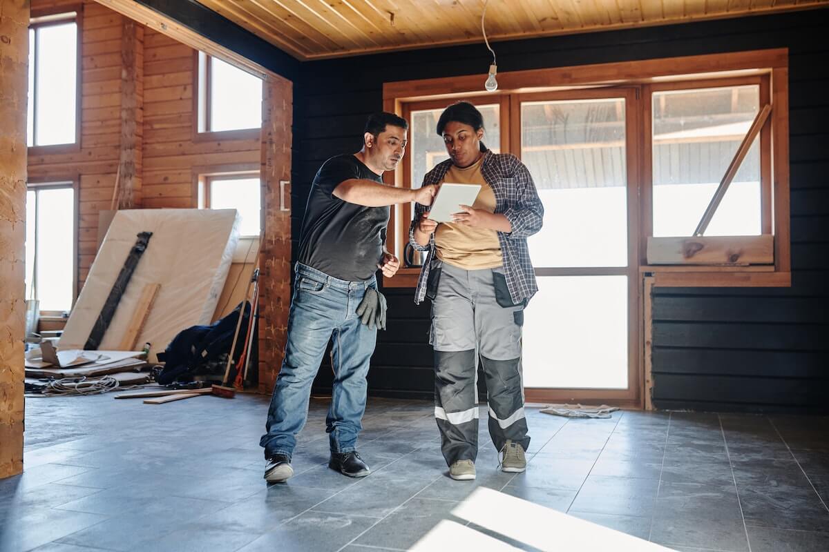 two workers reviewing specs in the middle of a room being renovated